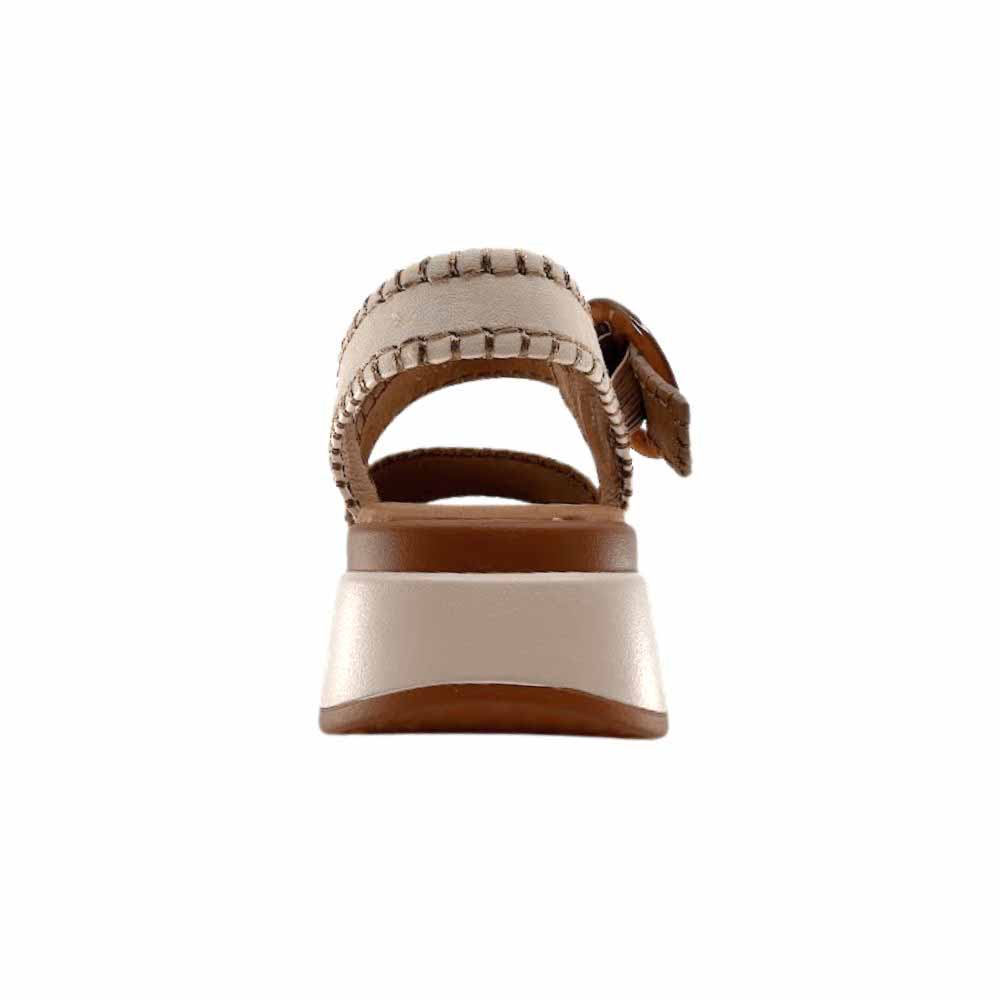 The back of a sandal with tan, taupe and cream leather straps with stitched edged detailing and a round buckle, set on a beige platform sole, against a white background.
