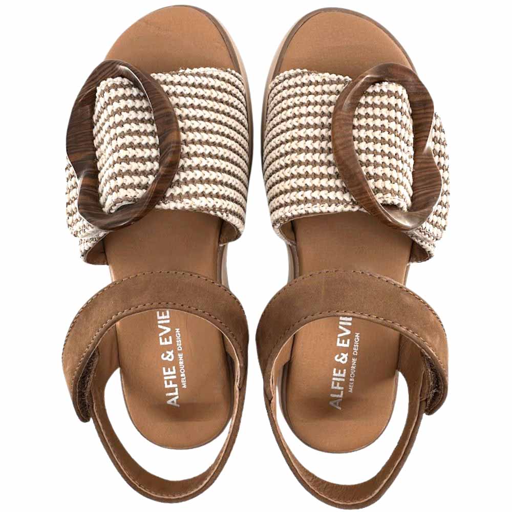 A pair of tan sandals with a tan and cream woven strap across the vamp showcasing a statement oversized buckle and tan ankle straps, shown from a top-down perspective against a white background.
