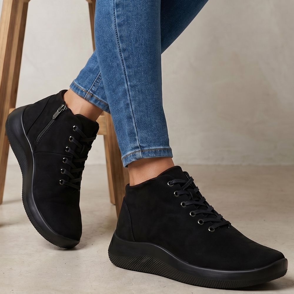 Person wearing black ankle boots with blue jeans on a neutral background