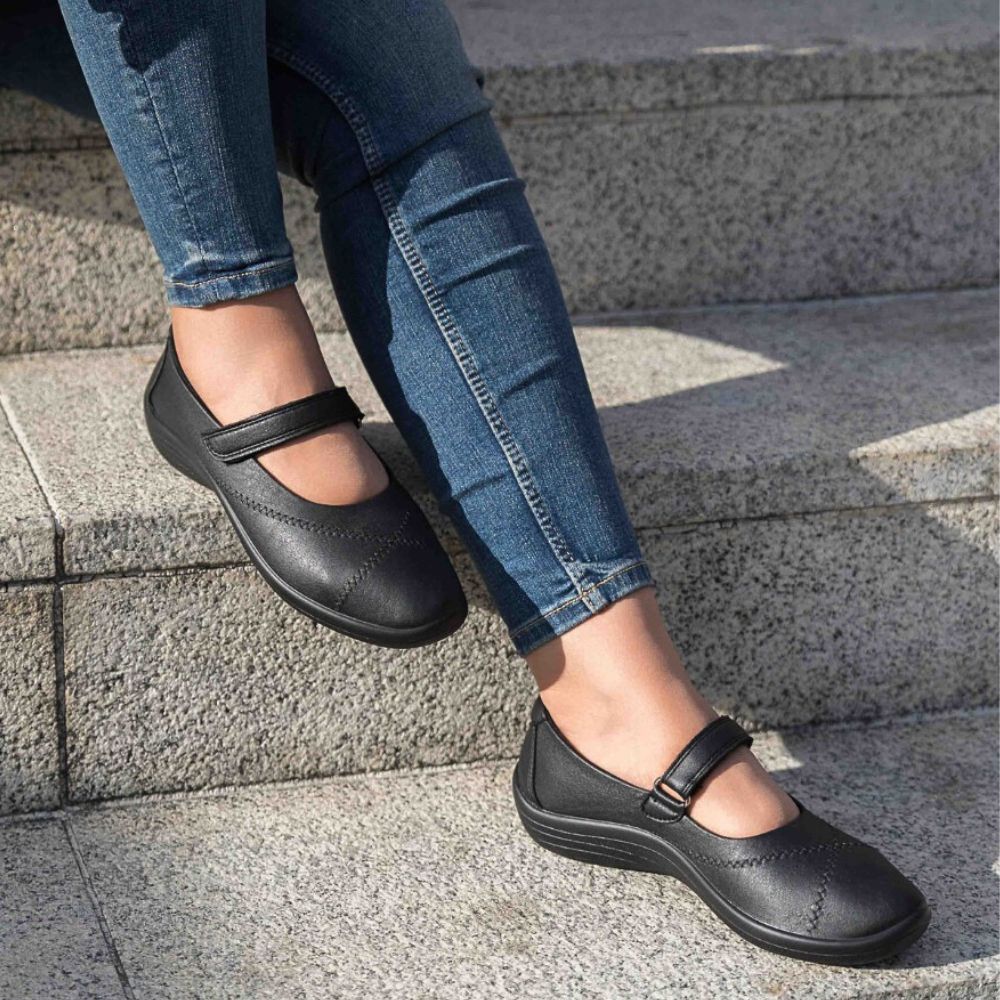Person wearing black Mary Jane shoes with strap on a stone step