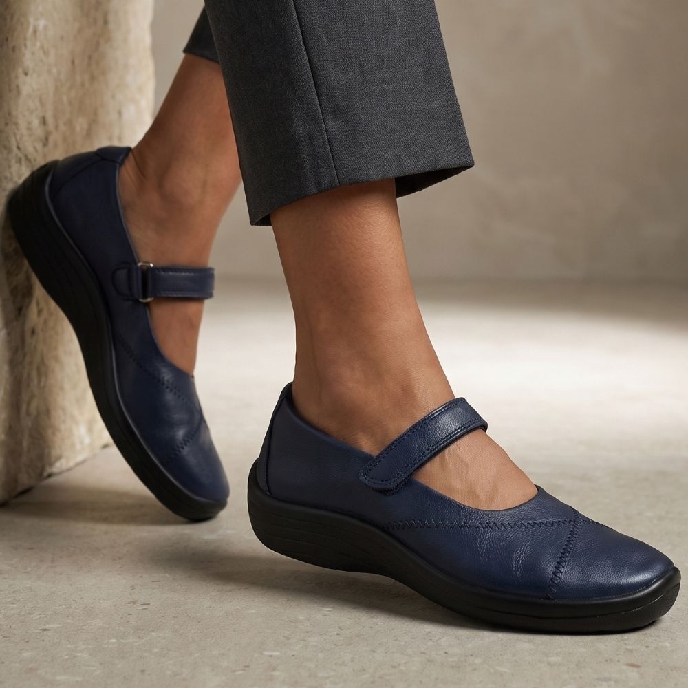 A person wearing navy blue 'Lytech' Mary-Jane style slip-on shoes with black soles, shown from the knees down against a neutral concrete and stone background.