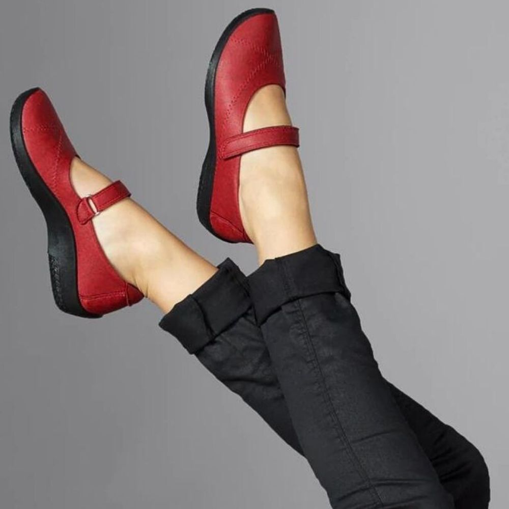 Red Mary Jane shoes with black soles worn by a person against a gray background