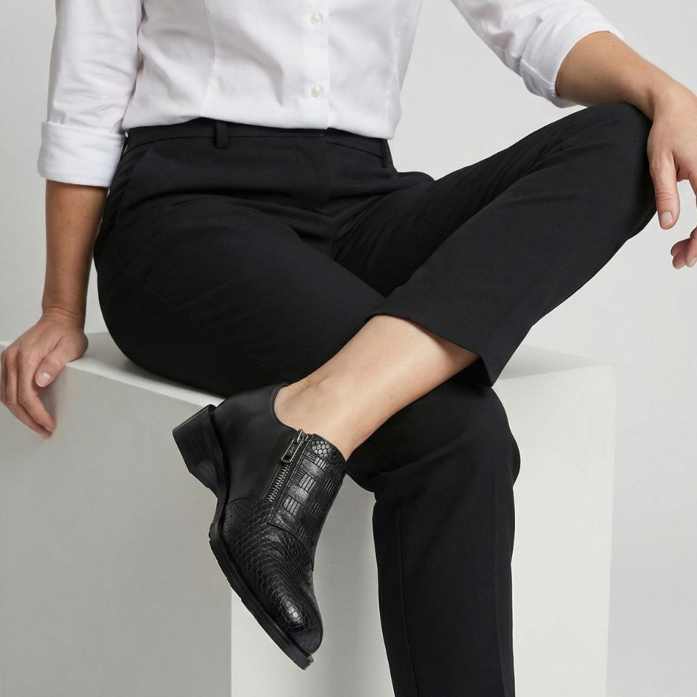 Person wearing black dress shoes and black pants sitting on a white surface.