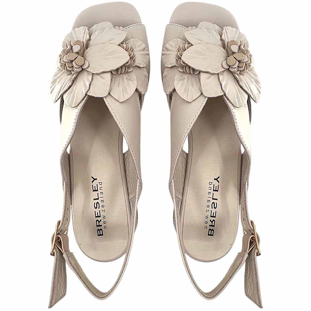 The top view of a pair of nude leather sandals with a floral leather embellishment across the vamp and peep toe, against a white background.