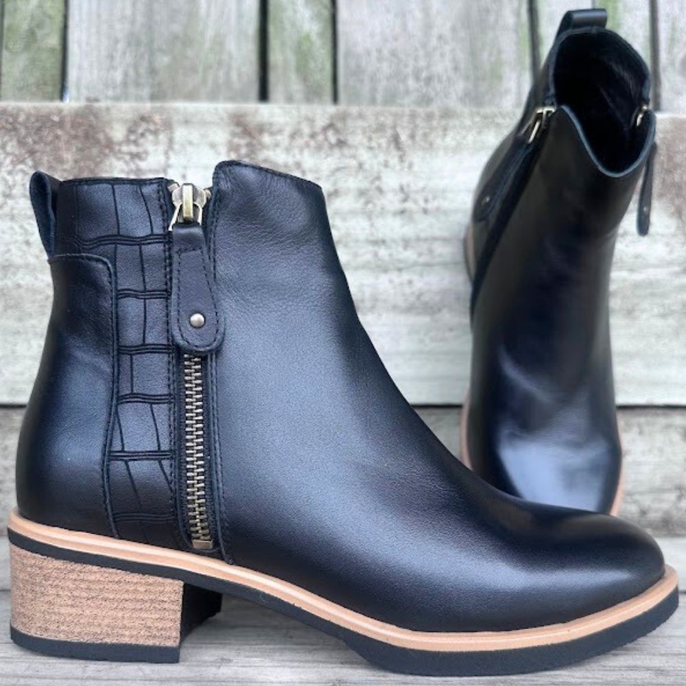 Black leather ankle boots with a wooden sole on a wooden surface.