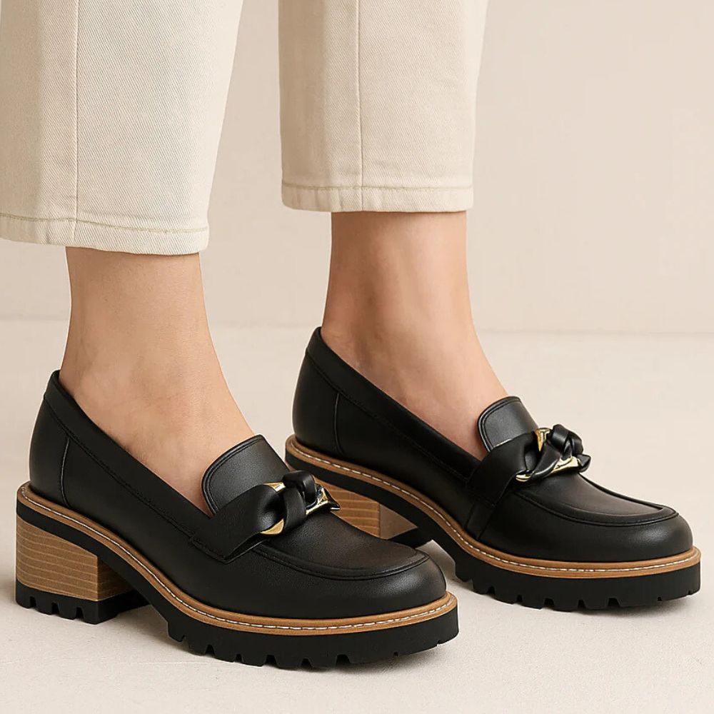Black loafers with wooden soles worn by a person on a neutral background