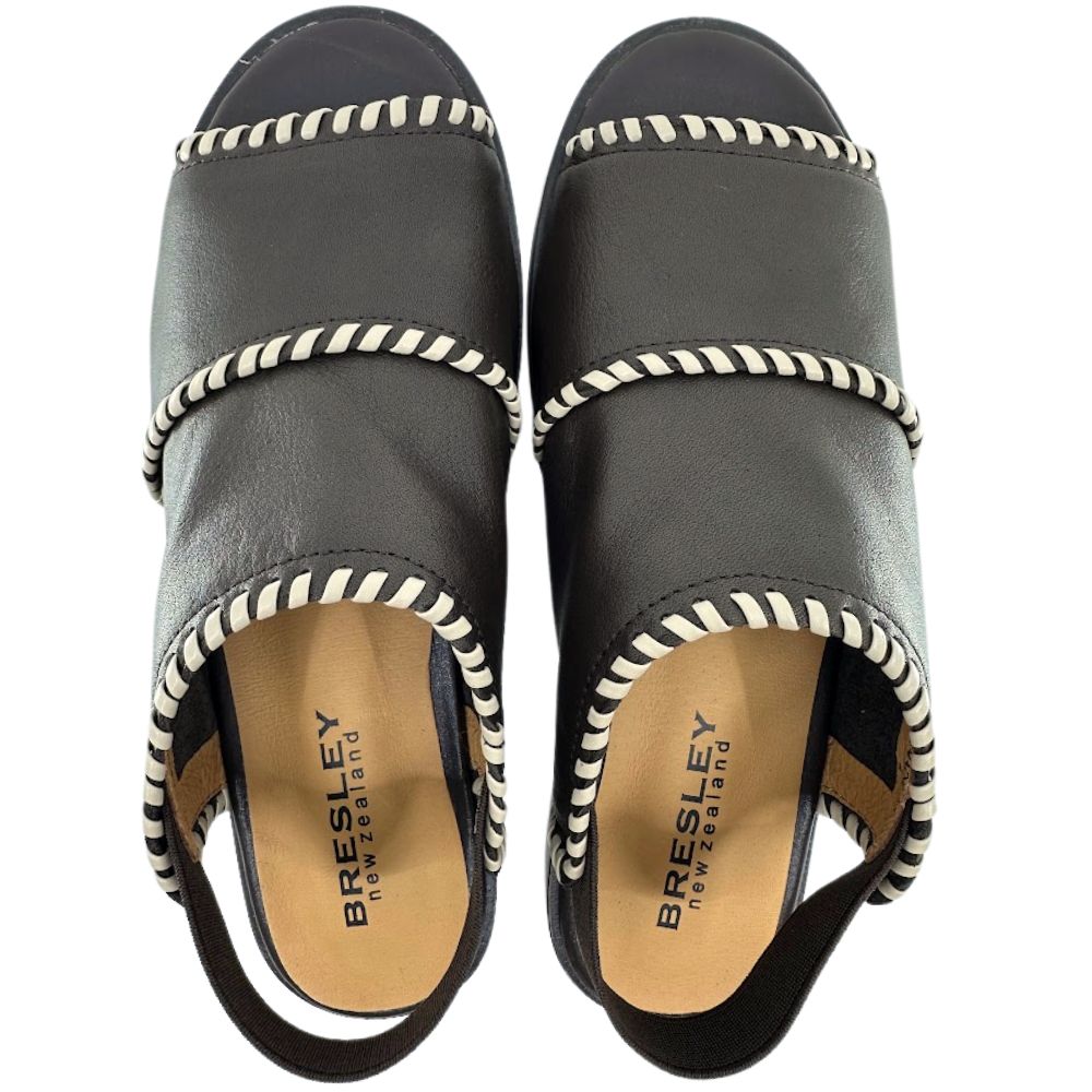 A pair of dark brown leather slide sandals by Bresley, featuring cream braided trim along the edges and a tan insole with the brand name printed in black.