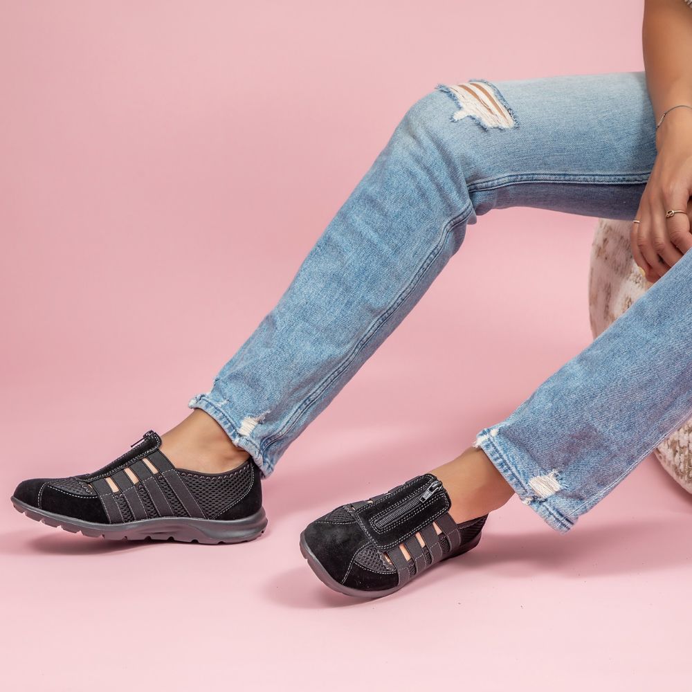 Person in blue jeans wearing black slip-on shoes on a pink background