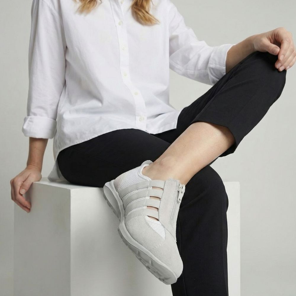 Person wearing cream sneakers and black pants sitting on a white surface.