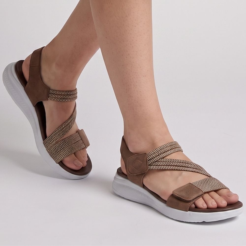 A person wearing dark brown leather and woven elastic strap sandals with thick white soles, shown in a side profile view against a white studio background.