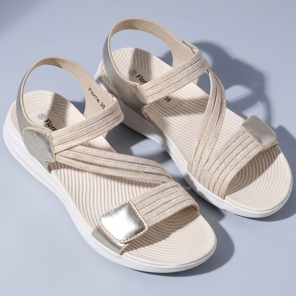 A pair of metallic champagne gold women's sandal with multiple elastic woven straps and thick white cushioned soles, shown in a top-down profile on a mauve background.