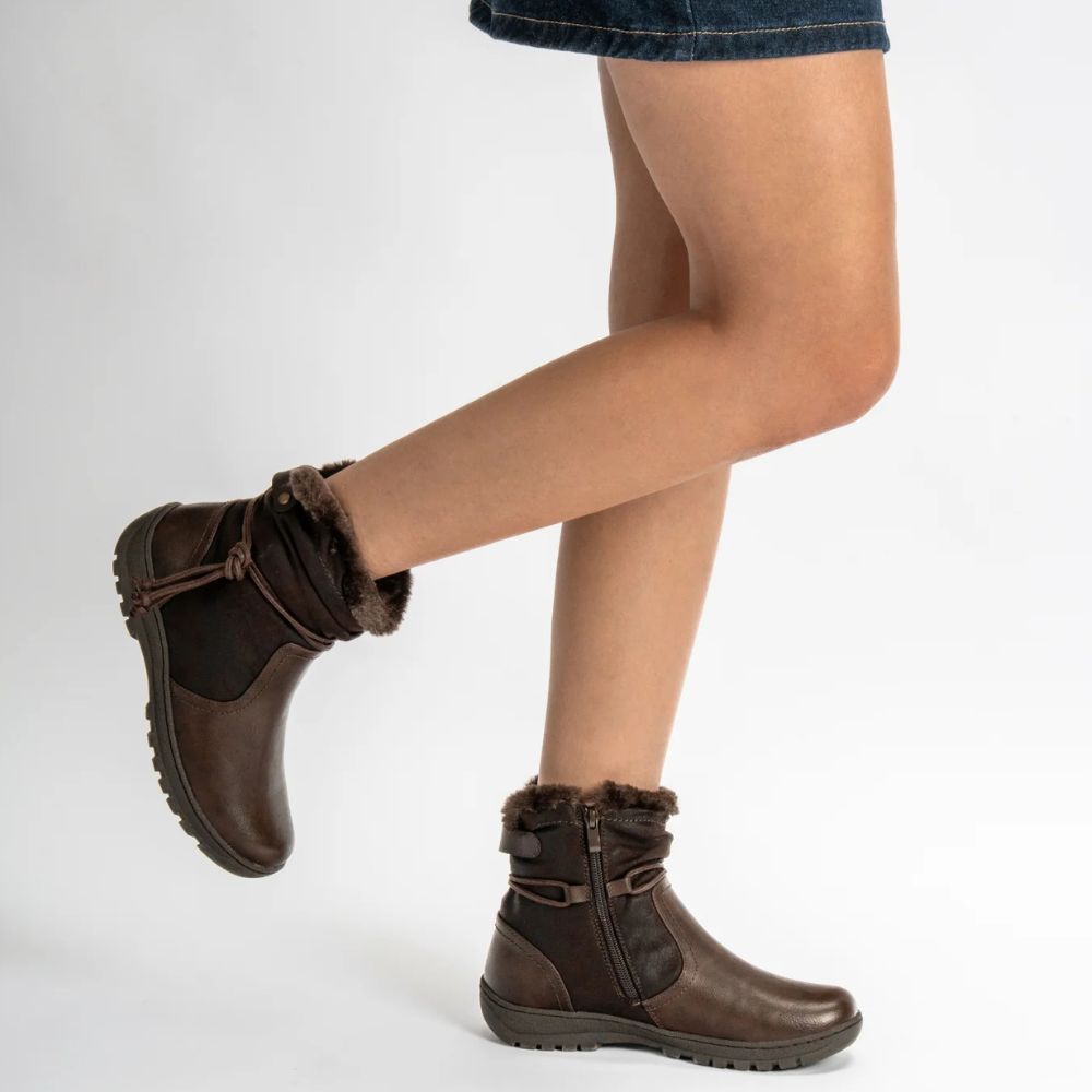 Brown ankle boots with fur trim worn by a person on a white background