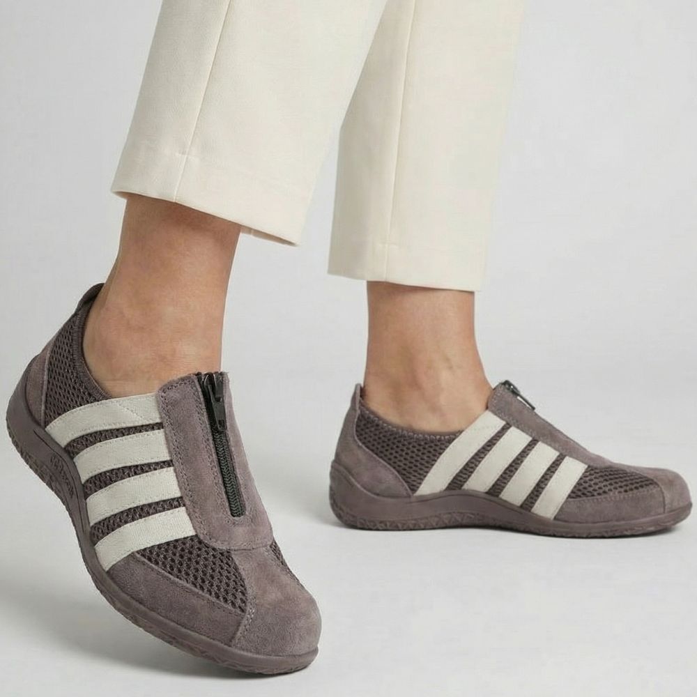 Brown slip-on shoes with cream stripes worn by a person on a light gray background