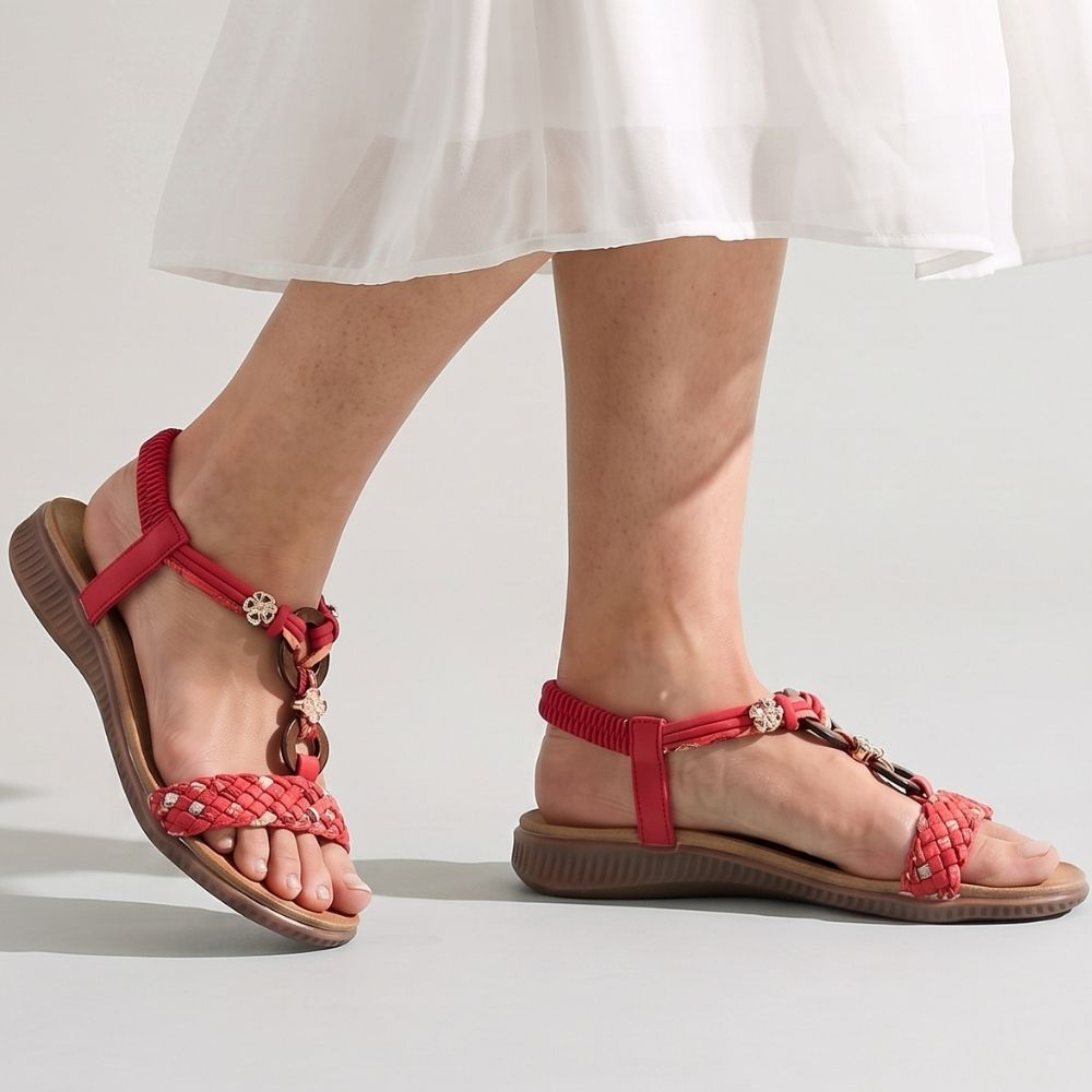 Red woven flat sandals with red woven straps and brown soles, shown on a model's feet against a light gray studio background.