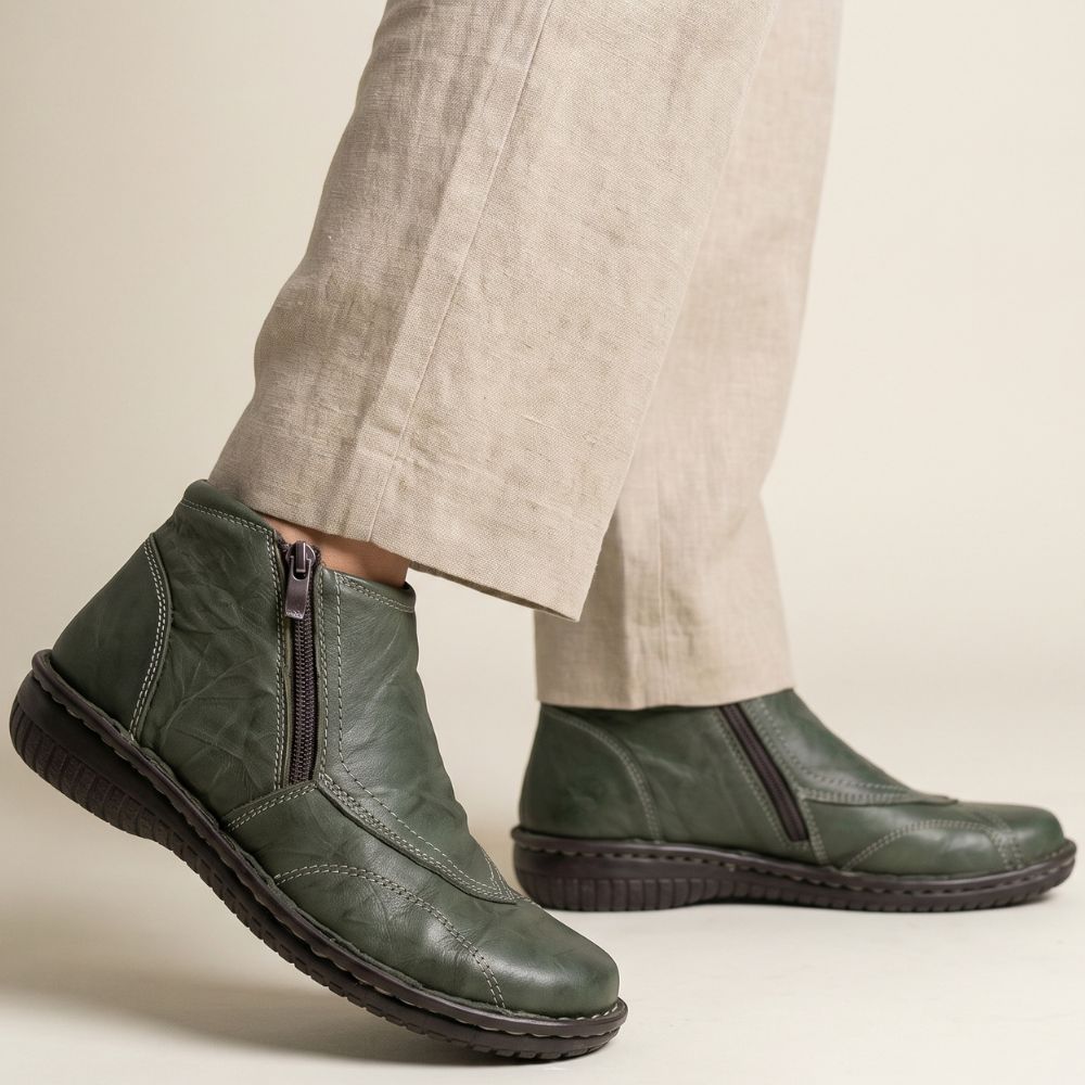 Khaki leather ankle boots worn with beige pants on a neutral background