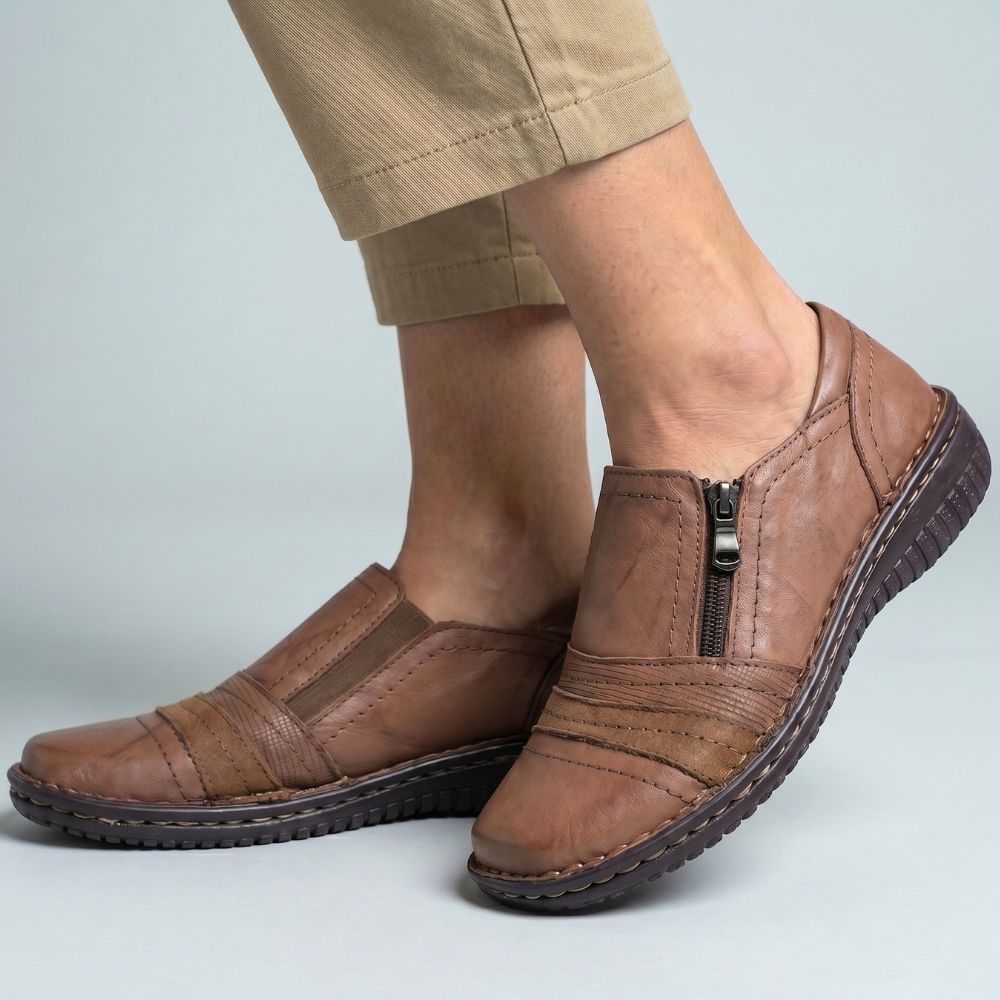 Brown leather shoes with zippers worn by a person on a light gray background