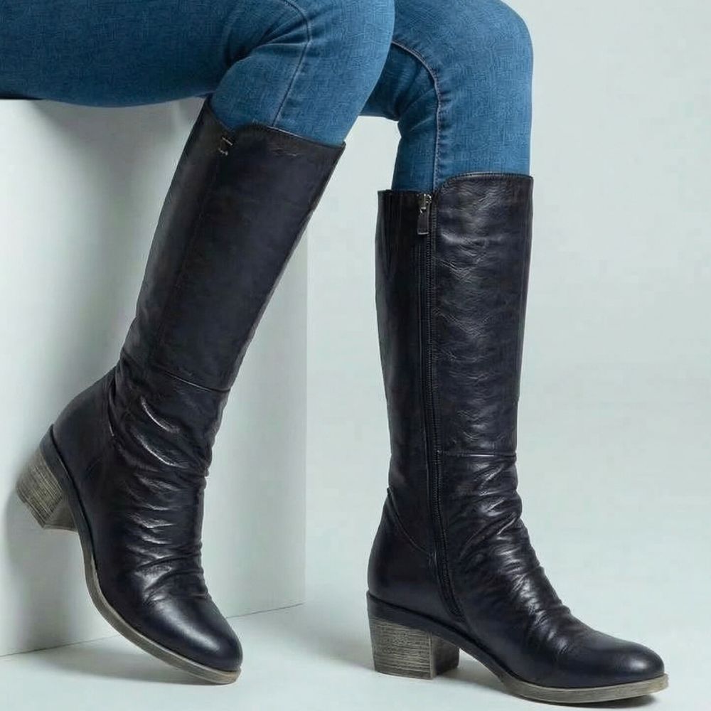 Black knee-high boots worn with blue jeans on a light gray background