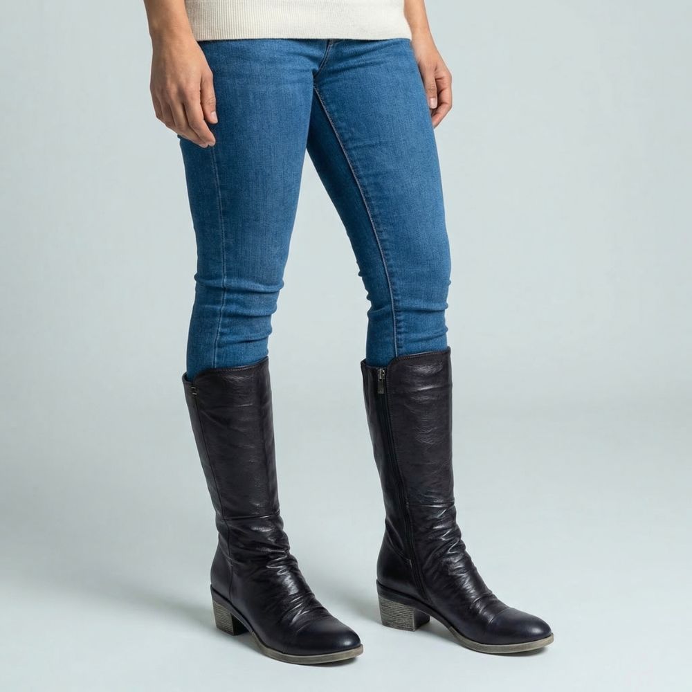 Person wearing blue jeans and black knee-high boots on a light gray background