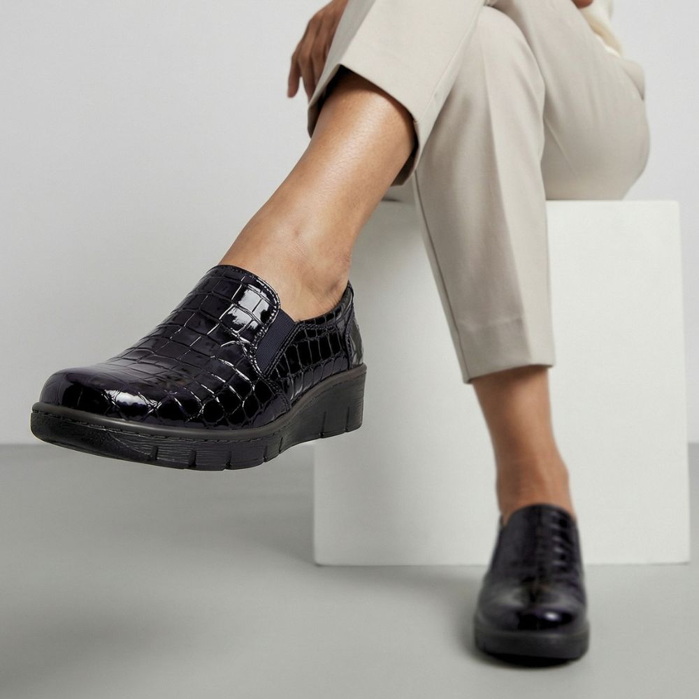 Person wearing black crocodile-patterned shoes on a light gray background