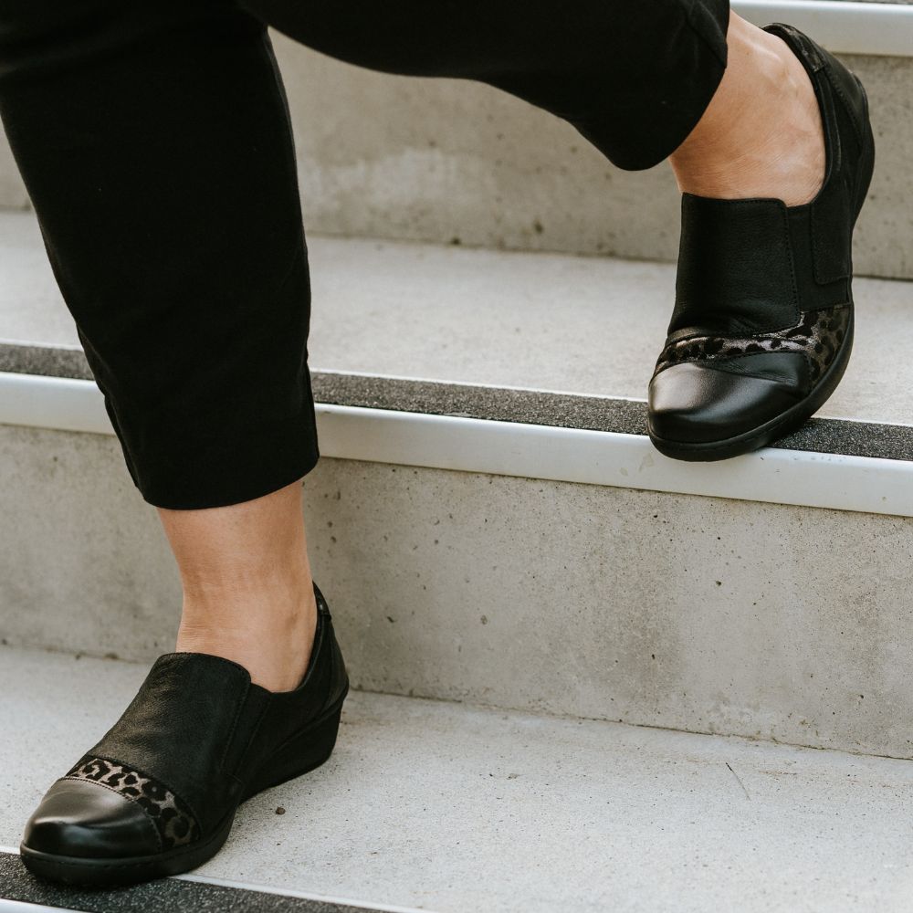 Person wearing black shoes with decorative toes on a concrete step.