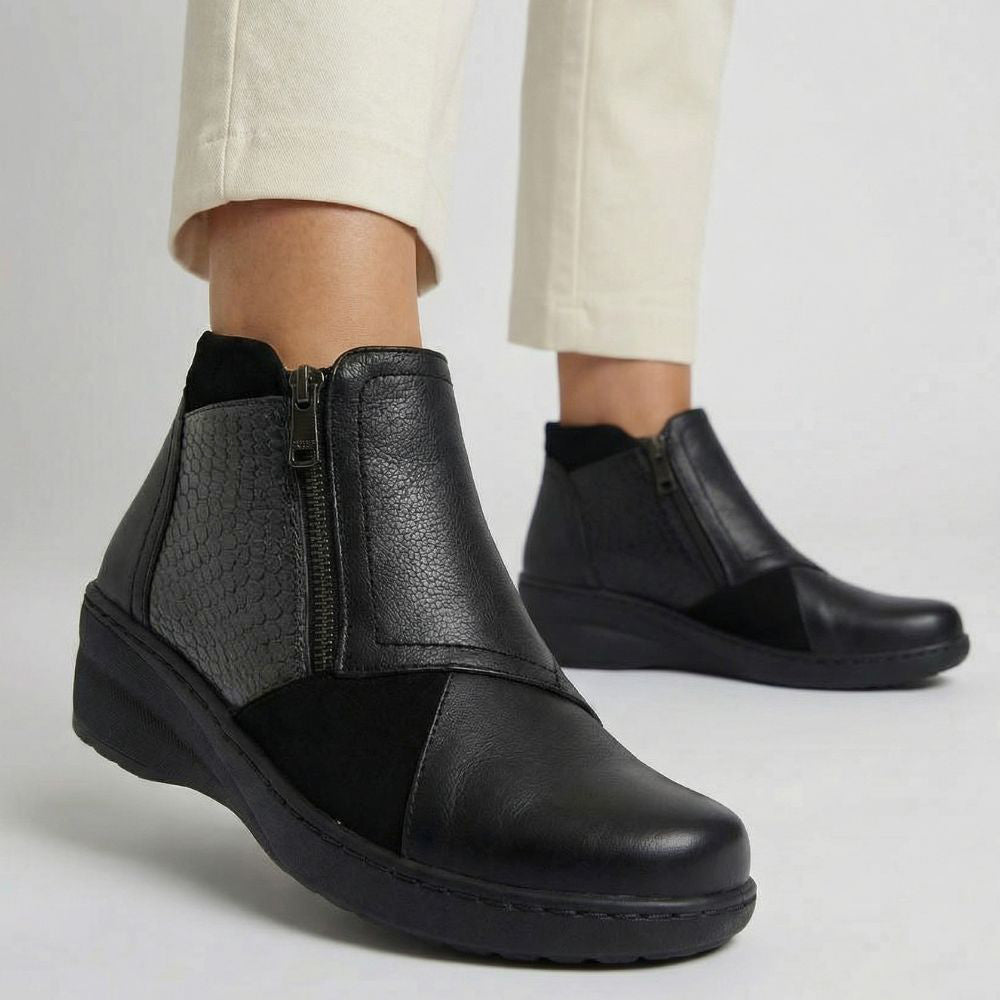 Black leather ankle boots worn with beige pants on a light gray background