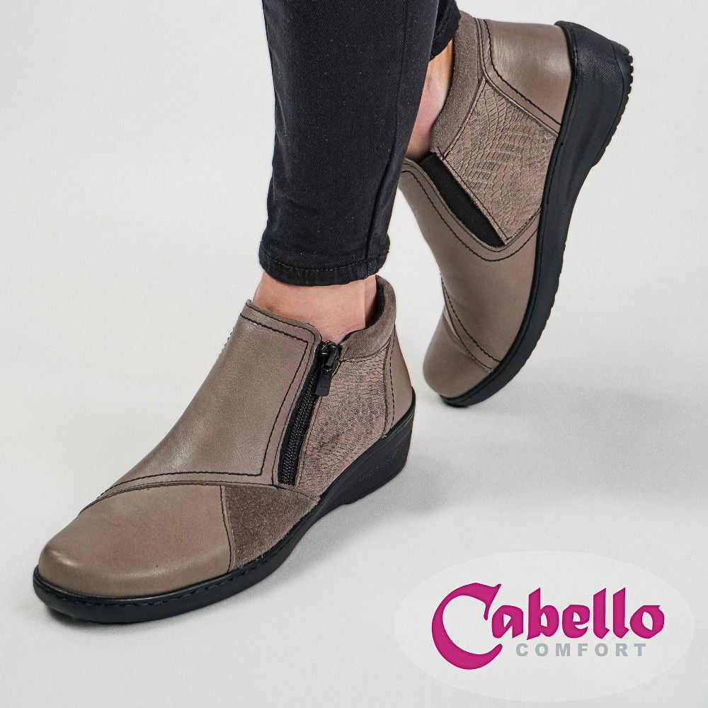 Taupe leather ankle boots with black soles worn by a person, on a light gray background with 'Cabello Comfort' branding.