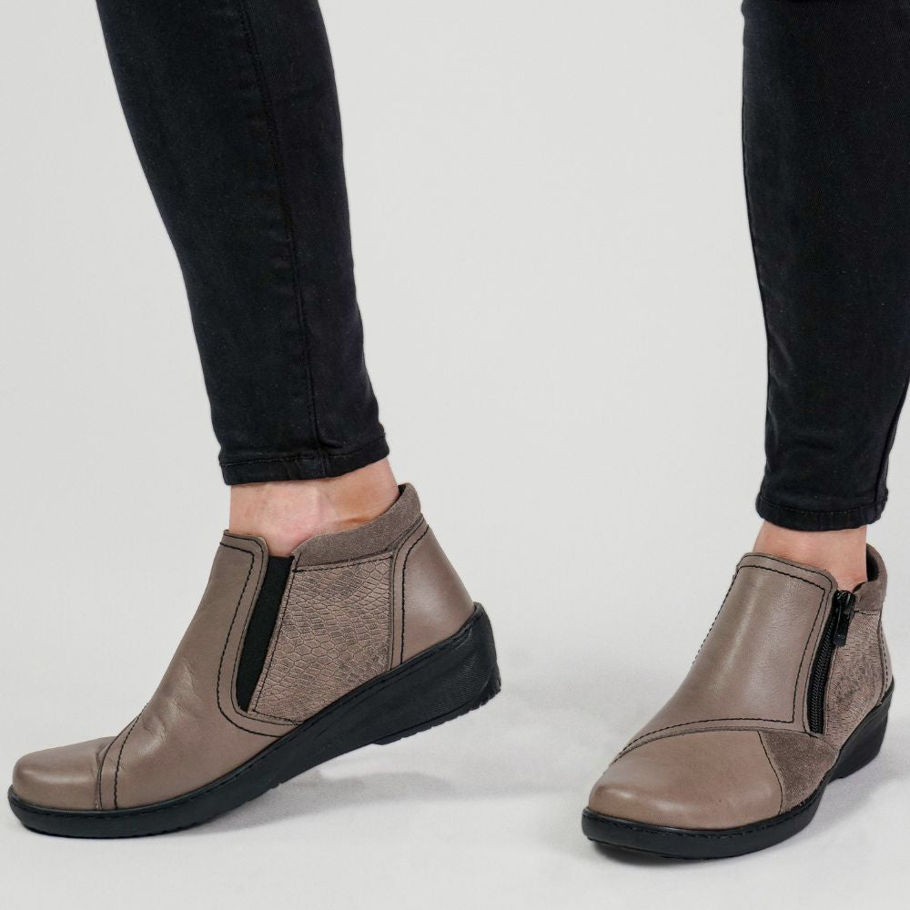 Taupe leather ankle boots worn with black pants on a light gray background