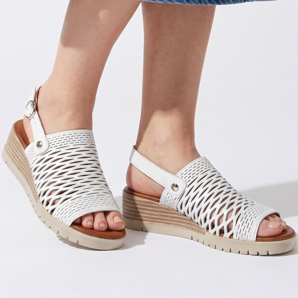 White woven open-toe wedge sandals with adjustable ankle straps, shown on a model's feet against a clean white background.