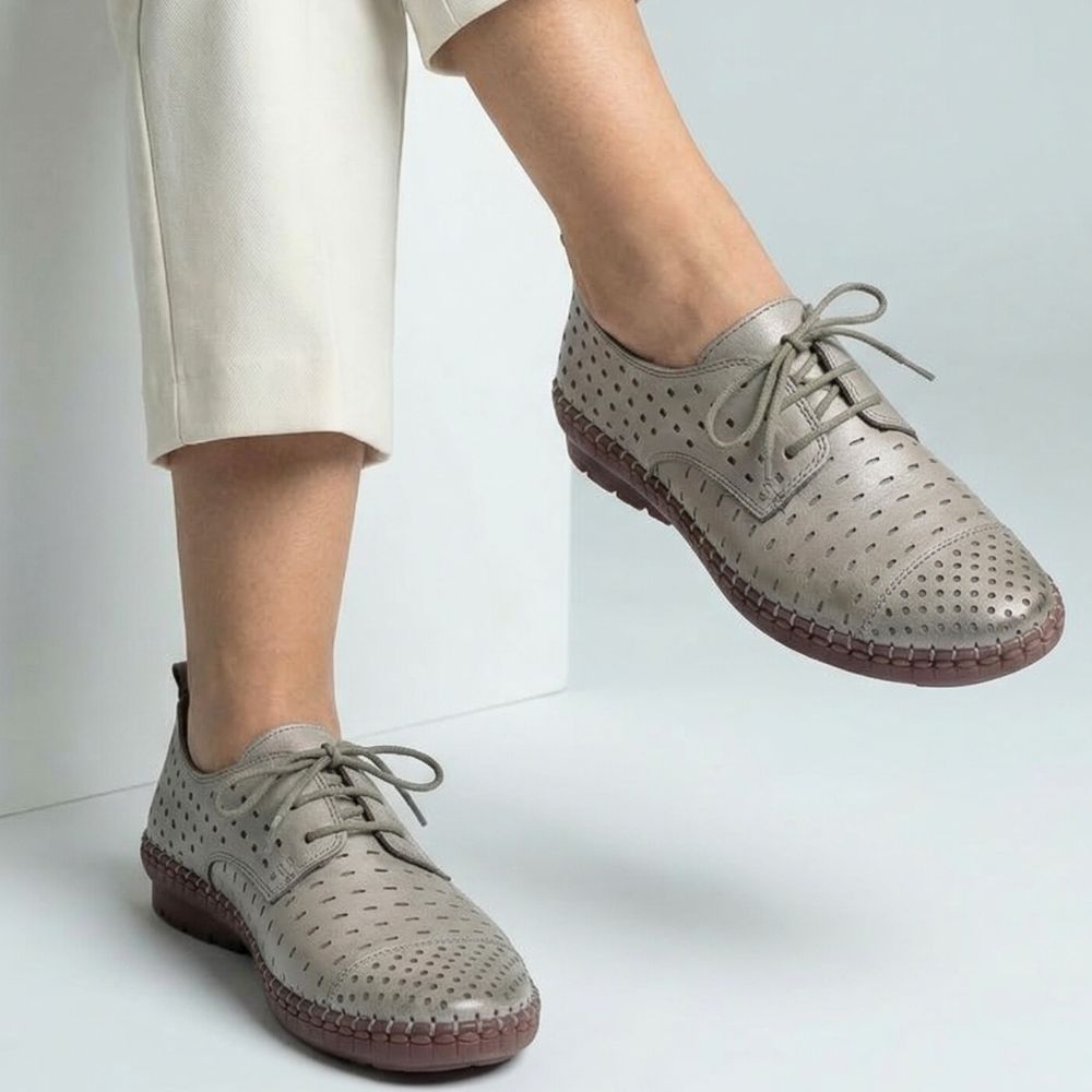 Taupe perforated shoes with brown soles worn by a person on a light gray background