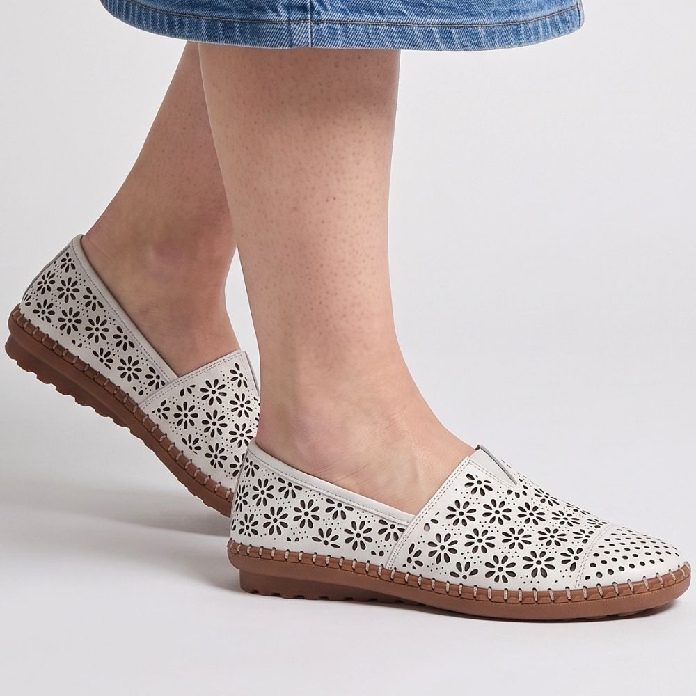 A person wearing a denim skirt wearing a pair of white laser-cut Cabello leather loafers with a central elastic gusset, shown against a studio background.