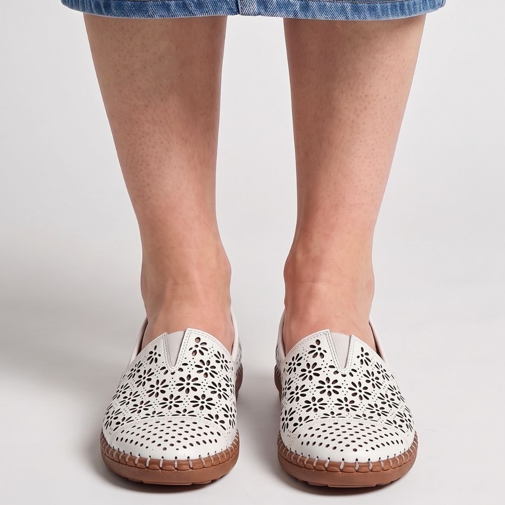 A person wearing a denim skirt wearing a pair of white laser-cut Cabello leather loafers with a central elastic gusset, shown from a front-on view, standing against a studio background.