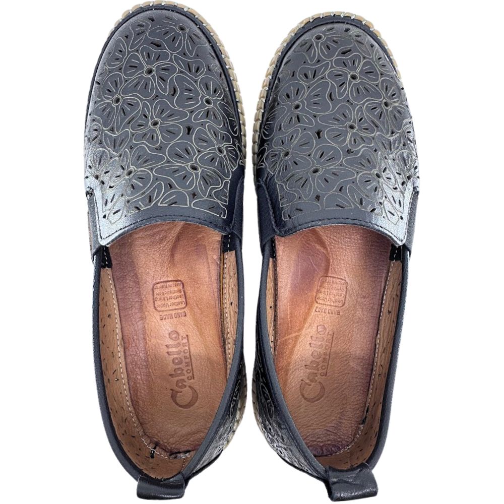 Pair of black slip on shoes with floral laser  cut pattern on a white background