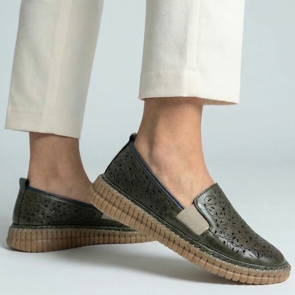 Olive slip-on loafer shoes with brown soles worn with beige pants on a light gray background