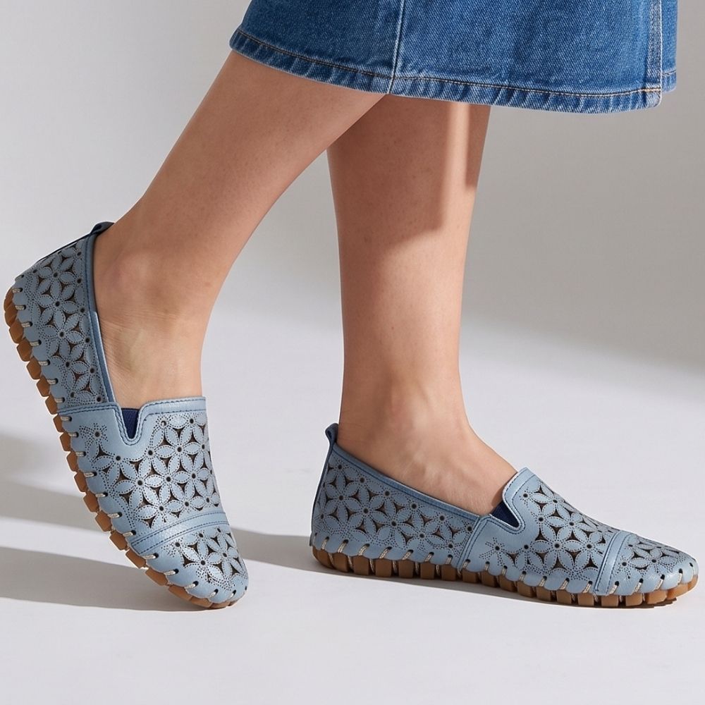 A lady in a denim skirt wearing a pair of denim blue laser-cut Cabello leather loafers with elastic gussets, shown against a studio background.