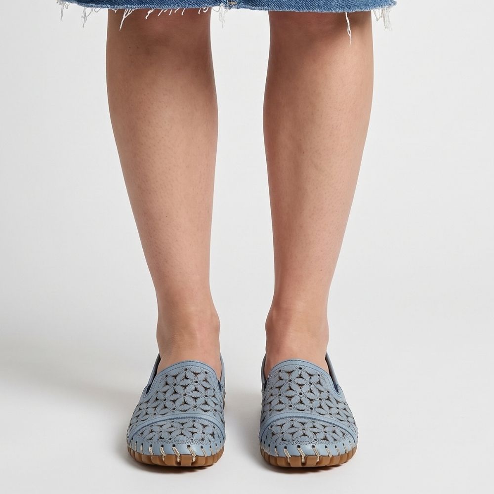 A lady in a denim skirt wearing a pair of denim blue laser-cut Cabello leather loafers with elastic gussets, shown from a front-on view against a studio background.