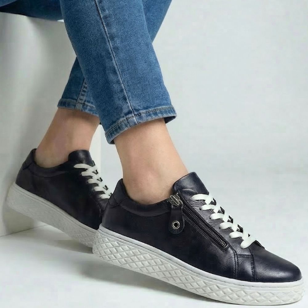 Black sneakers with white soles worn with blue jeans on a light gray background
