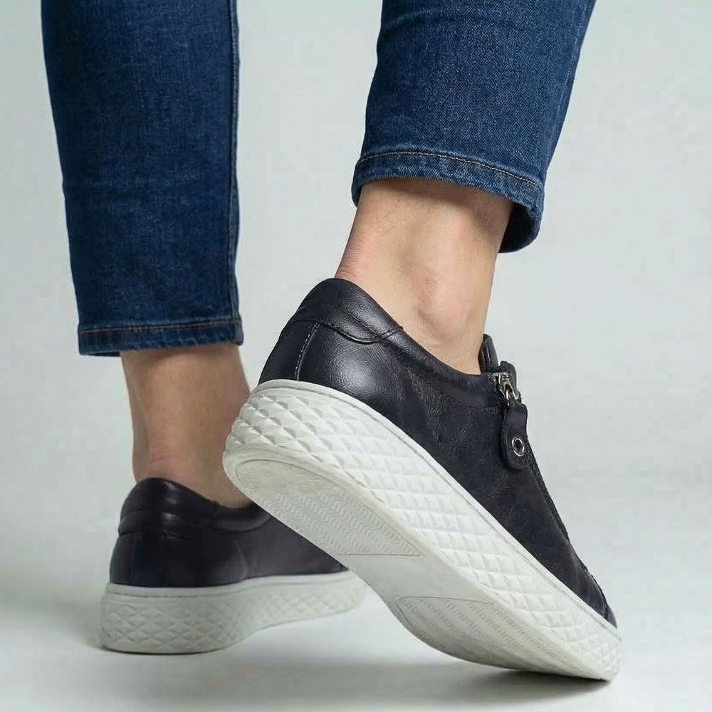 Black sneakers with white soles worn with blue jeans on a light gray background