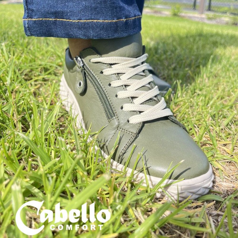 Person with blue jeans, standing on grass wearing khaki sneakers with zip and laces 