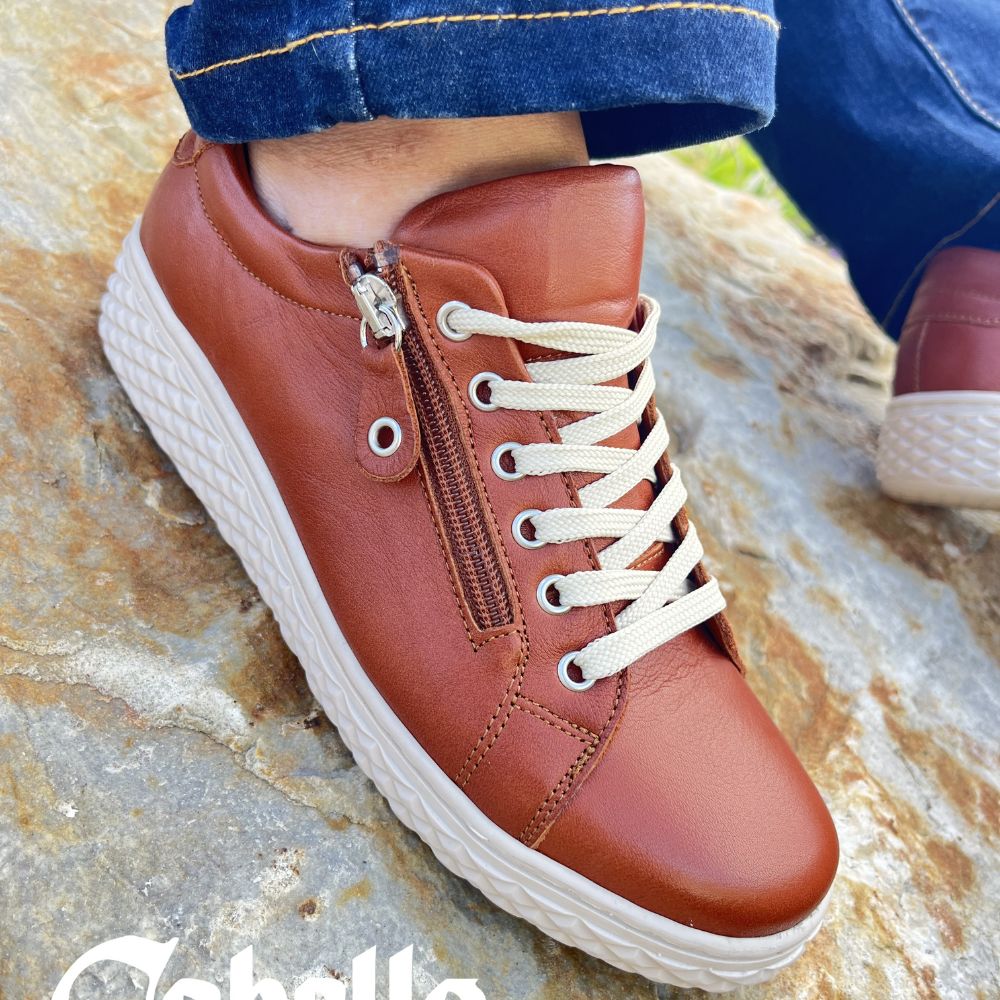 Person wearing blue jeans and tan sneakers with zip entry and lace up adjustment on a rock