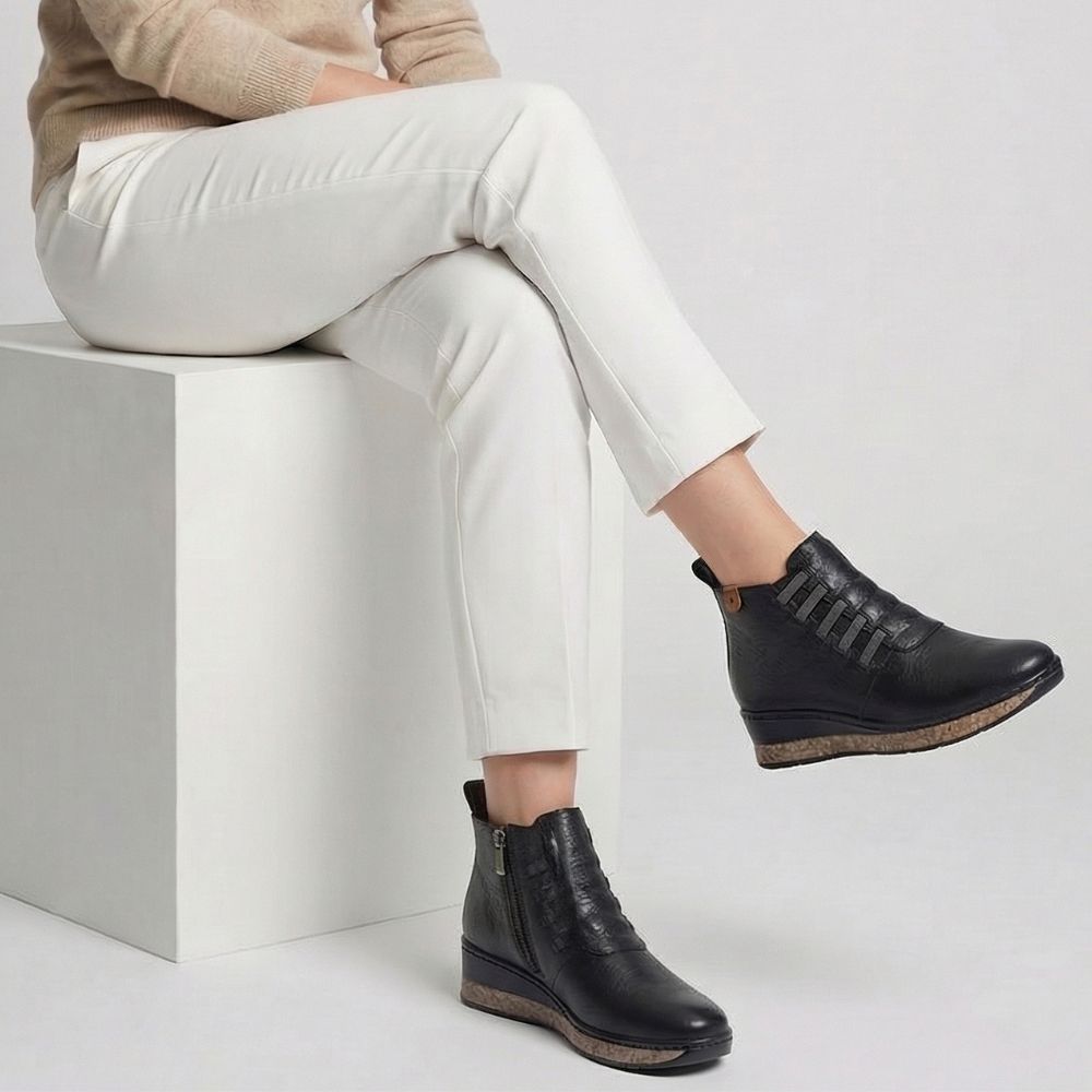 Person wearing black leather boots sitting on a white block with a light gray background
