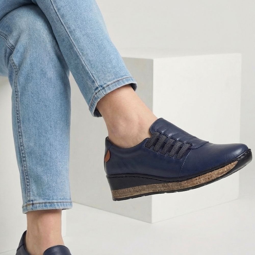 Navy blue shoe with cork sole worn by a person sitting on a white step.