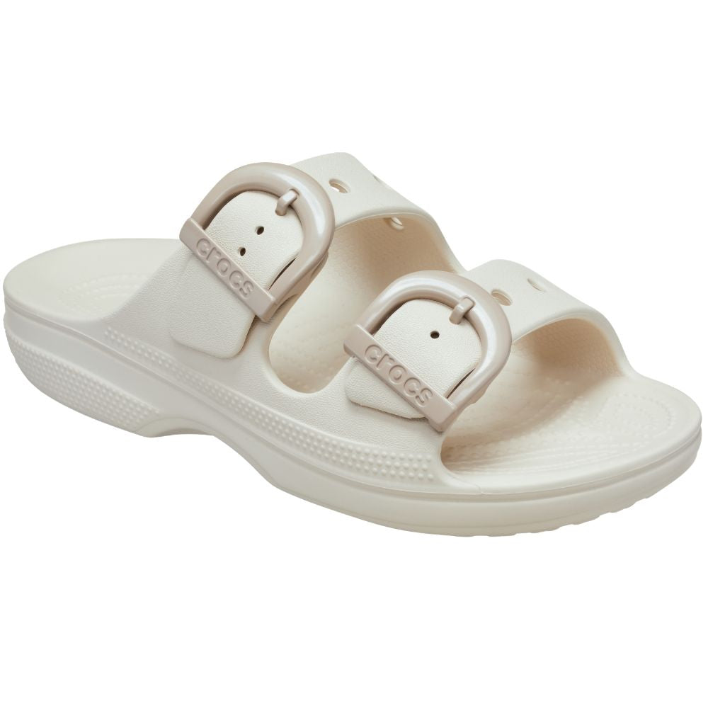 A single Crocs double-strap slide sandal in a warm off-white or cream color, featuring two adjustable straps with taupe enamel buckles and the Crocs logo embossed on them, set against a plain white background.