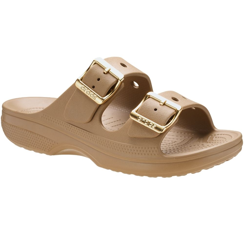 A tan double-strap 'Crocs' slide sandal with gold-tone buckle hardware, shown from a three-quarters angle on a white background.