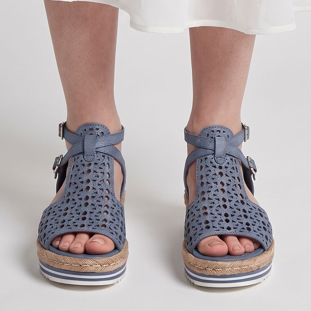 A pair of women's platform wedge sandals in a denim blue color, featuring a textured woven espadrille-style sole and adjustable ankle straps with silver buckles, shown on a model's feet against a light gray background.
