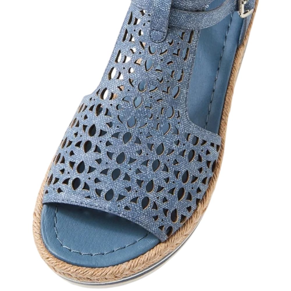 A close-up of a blue denim leather wedge sandal with a floral cutout pattern on the upper, a braided jute espadrille sole, and a blue insole.