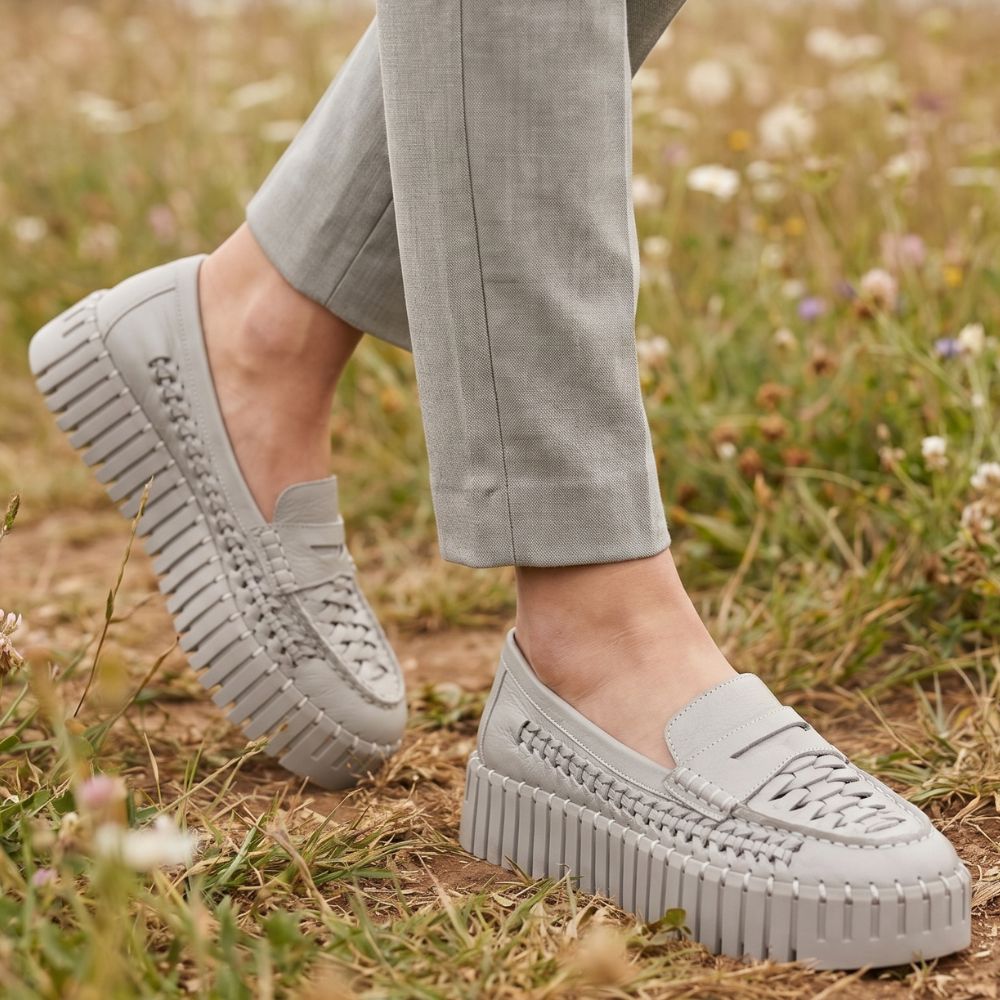 Person walking through field wearing grey pants and taupe woven leather loafers with a platform sole
