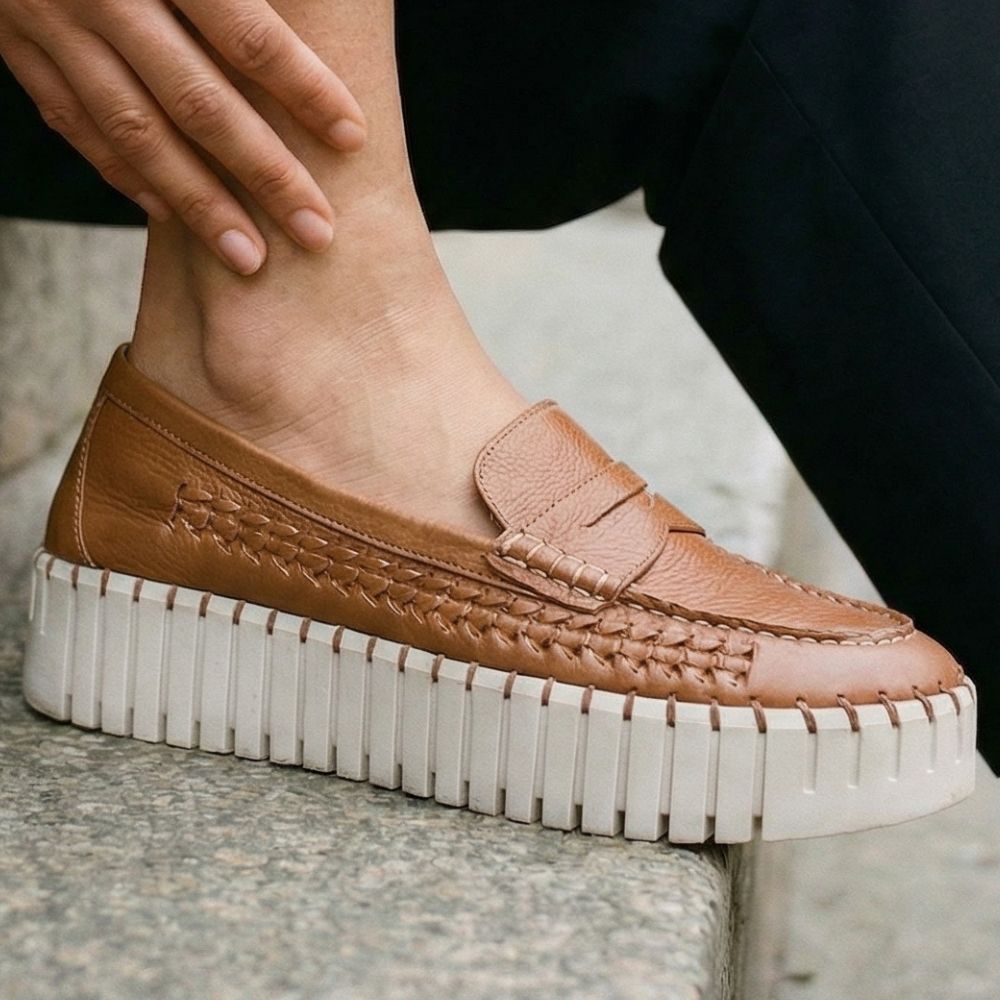Tan woven leather loafer with thick white sole worn by a person.