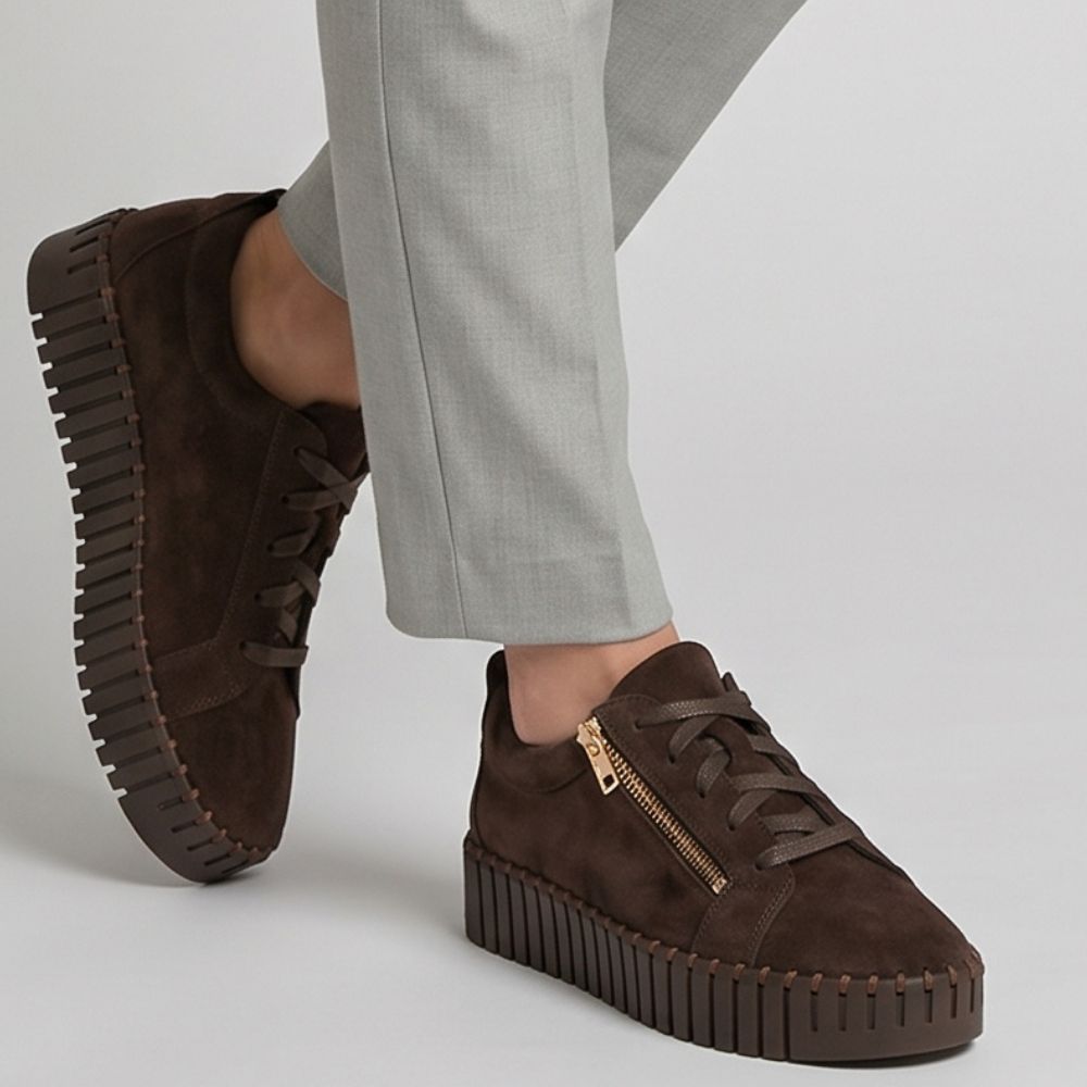 Brown suede sneakers with a platform sole worn with light gray pants on a neutral background
