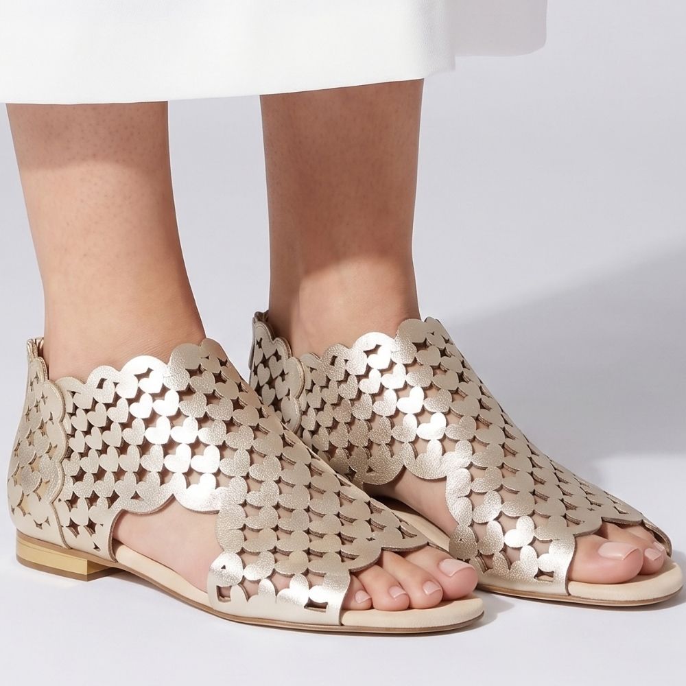 A pair of women's flat sandals with an intricate cutout pattern of hearts, shown on a model's feet against a clean white background.