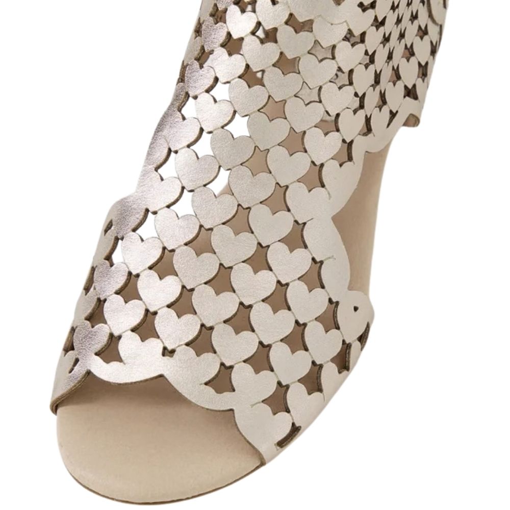 A close-up of a metallic gold peep-toe sandal with a repeating heart-shaped cutout pattern on the upper and a beige insole.